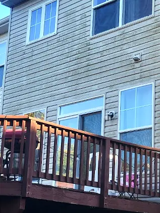 Before: Rear of a townhouse with green algae streaking across the vinyl siding above a deck